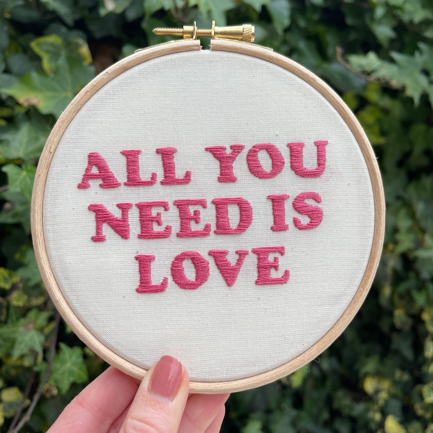 Embroidery hoop with white fabric and pink hand embroidered Beatles lyric All you need is love